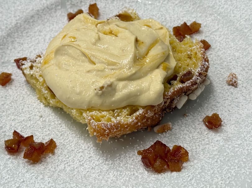 A dessert of panettone with creamy mascarpone, candied fruit, and powdered sugar on a white plate.